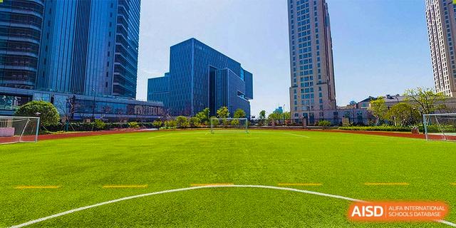 A large, green sports field next to a modern high-rise building on the campus of BASIS International School Hangzhou (BIHZ).