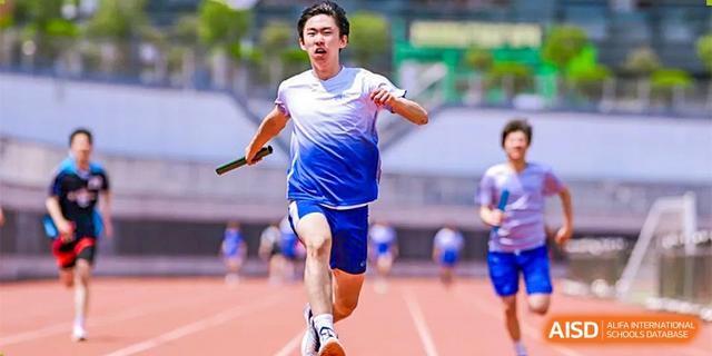 A male student in a white and blue uniform sprinting and holding a baton during a track relay race at BASIS International School Hangzhou (BIHZ).