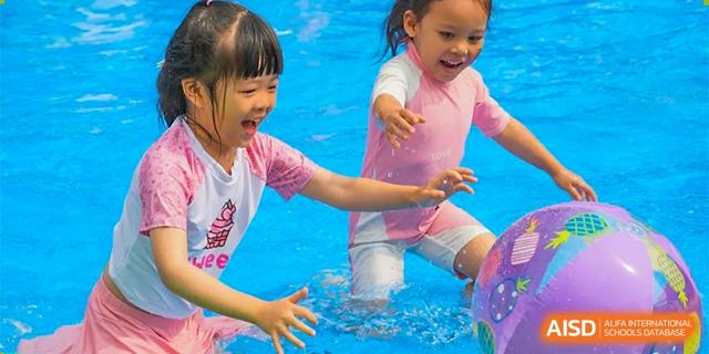 Two young female students smiling and splashing while playing in a shallow pool or water area at BASIS International School Hangzhou (BIHZ).