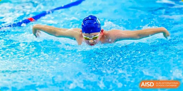 A male student wearing a swimming cap and goggles performing the freestyle stroke in a swimming pool at BASIS International School Hangzhou (BIHZ).