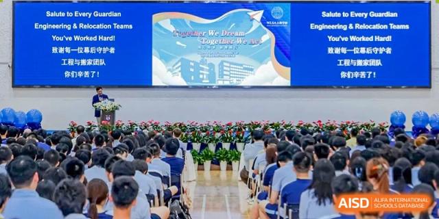 A large group of students from World Leading Schools Association seated for an assembly beneath a large screen with event graphics.