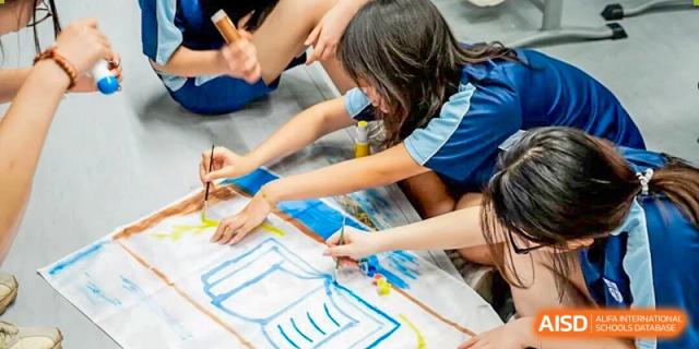 Two female students from World Leading Schools Association working on a colorful, large-scale painting or art project on the floor.