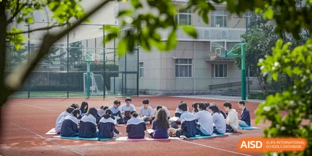 A group of students from World Leading Schools Association sitting in a circle outdoors on a sports track, socializing or having a discussion.