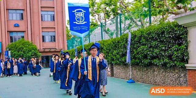 A graduating student from World Leading Schools Association in a cap and gown waving while marching outdoors in a procession.