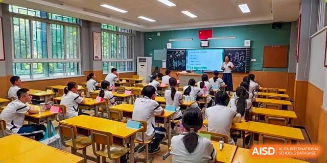 Zhengzhou No.9 High School International Department students attending a lesson in a bright classroom with small yellow and orange desks.