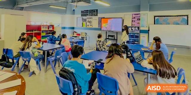 Students working together at a blue table in a classroom, possibly on a group project, at QSI International School of Dongguan.