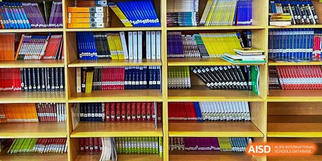 Shelves stacked with neatly organized binders and books in various colors, likely in a classroom or library, at QSI International School of Dongguan.