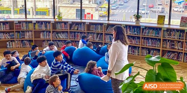 Students and an adult seated on blue bean bag chairs in the school library or reading area at QSI International School of Dongguan.