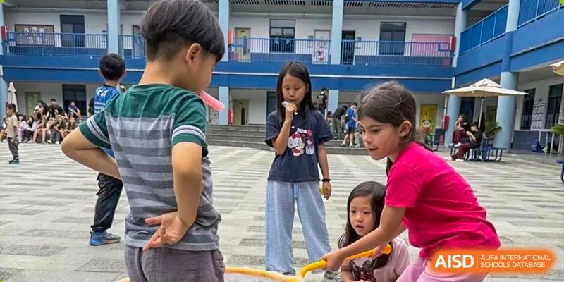 Students participating in a school fair or outdoor activity on the steps and paved area of the campus at QSI International School of Dongguan.