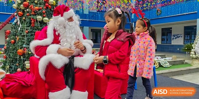 A young student in a red jacket standing next to a person dressed as Santa Claus during a holiday event at QSI International School of Dongguan.