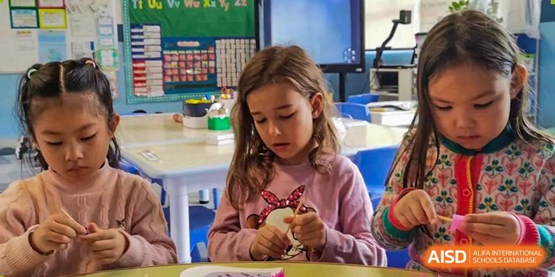 A young female student focused on a hands-on craft or activity in a bright classroom at QSI International School of Dongguan.