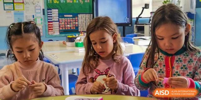 A young female student focused on a hands-on craft or activity in a bright classroom at QSI International School of Dongguan.