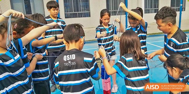 Students in blue and black sports uniforms walking outdoors, with one student holding a lanyard, at QSI International School of Dongguan.