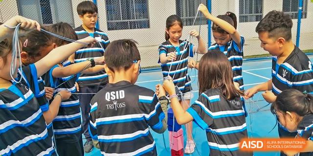 Students in blue and black sports uniforms walking outdoors, with one student holding a lanyard, at QSI International School of Dongguan.