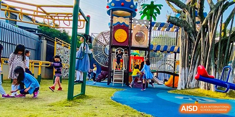 Children playing on a colorful outdoor playground structure with slides and ropes on a green and blue surface at QSI International School of Dongguan.