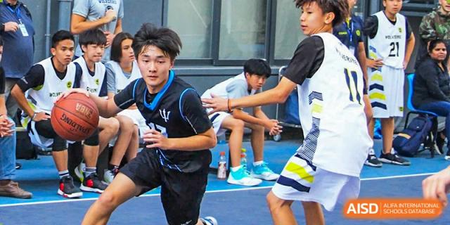 Male students in sports jerseys participating in an outdoor physical activity or game on a blue court at QSI International School of Dongguan.