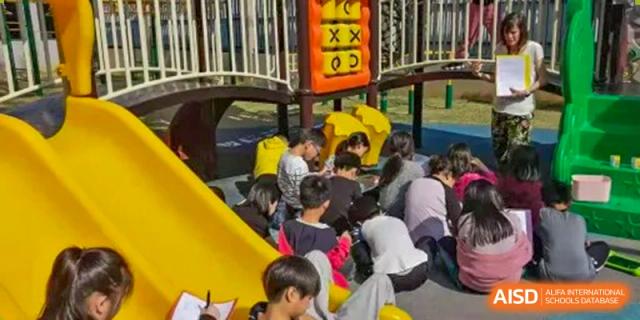 Children playing near a yellow slide on the playground during an outdoor recess or event at QSI International School of Dongguan.