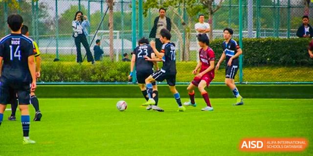 Students playing a soccer game on a green field, with two players competing for the ball, at QSI International School of Dongguan.