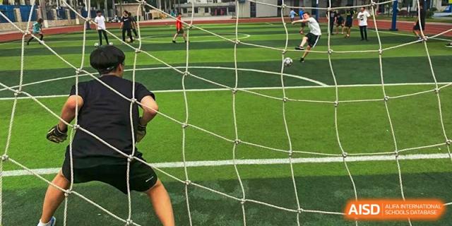 A close-up view of a soccer goal net on a synthetic turf field while students are playing a game at QSI International School of Dongguan.