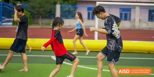 A close-up of students playing an outdoor game like soccer or rugby on a green field at QSI International School of Dongguan.