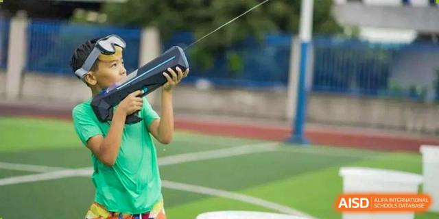 A student in a green shirt holding a rugby ball over their head during an outdoor sports activity at QSI International School of Dongguan.