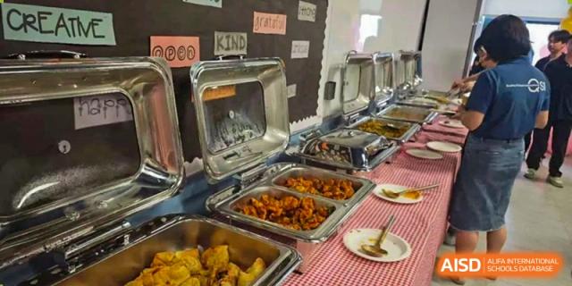 A chafing dish and serving tray filled with hot food, including golden-brown items and curry-like dishes, for a school meal at QSI International School of Dongguan.