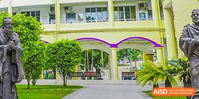 The entrance or campus grounds of Guangzhou Huamei International School, featuring green trees, benches, and a building with yellow and purple accents.