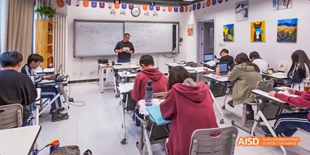 A teacher in a black shirt standing by a whiteboard and instructing students seated at desks. Beijing No.4 High School International Courses Jialian Campus.
