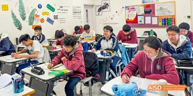 A group of students wearing maroon hooded sweatshirts studying intently at their desks in a classroom. Beijing No.4 High School International Courses Jialian Campus.