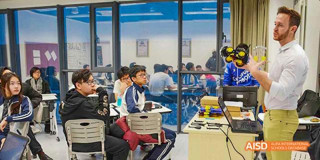 Students sitting at desks in a bright classroom with large windows, working on an activity or test. Beijing No.4 High School International Courses Jialian Campus.