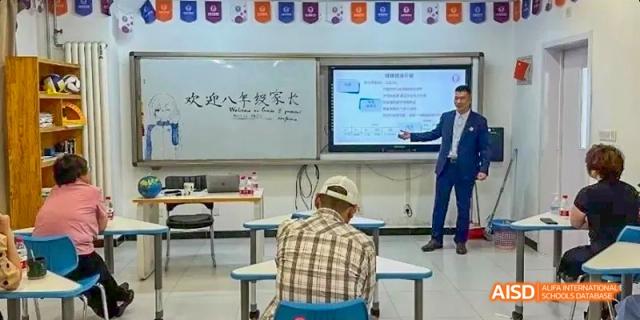 A student seated facing the back of the classroom where a lesson is being projected onto an interactive whiteboard. Beijing No.4 High School International Courses Jialian Campus.