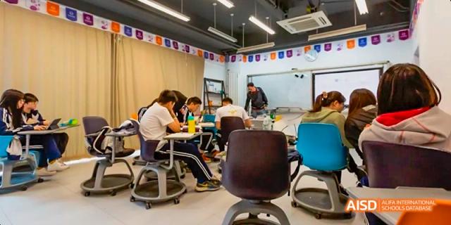 A group of students collaborating and working together at tables in a laboratory or hands-on classroom. Beijing No.4 High School International Courses Jialian Campus.