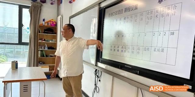 A male teacher pointing to a large interactive whiteboard displaying a Chinese calendar or chart. Beijing No.4 High School International Courses Jialian Campus.