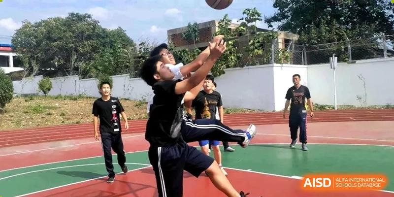 A student in a black shirt and shorts attempts a basketball layup on an outdoor court. Beijing No.4 High School International Courses Jialian Campus.