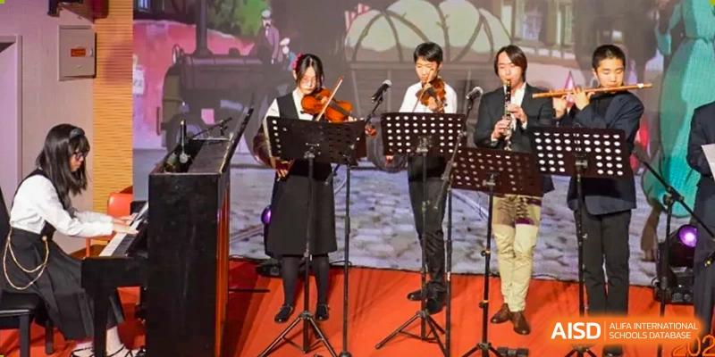 Two students playing string instruments—one violin and one cello or viola—on stage. Beijing No.4 High School International Courses Jialian Campus.