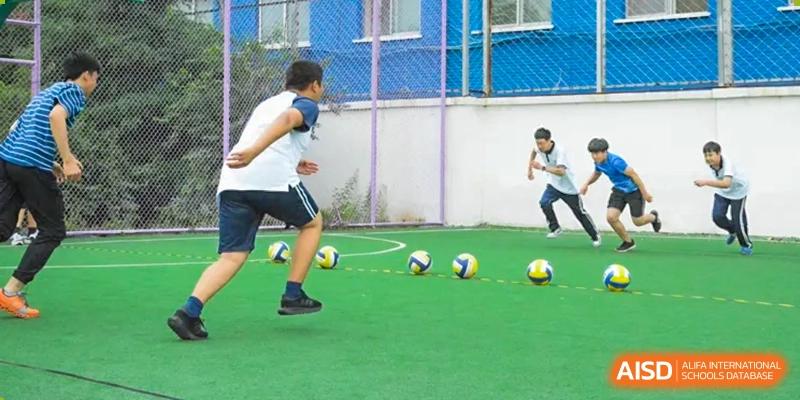 A student practicing a soccer kick or dribbling drill with several yellow soccer balls on a turf field. Beijing No.4 High School International Courses Jialian Campus.