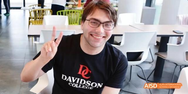 A smiling man wearing glasses and a black T-shirt that says "Davidson College." Beijing No.4 High School International Courses Jialian Campus.