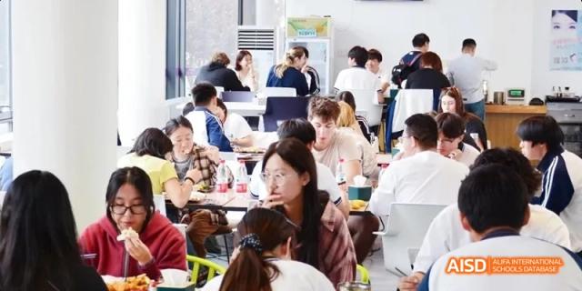 Students sitting and talking at tables in a busy, modern cafeteria or dining hall. Beijing No.4 High School International Courses Jialian Campus.