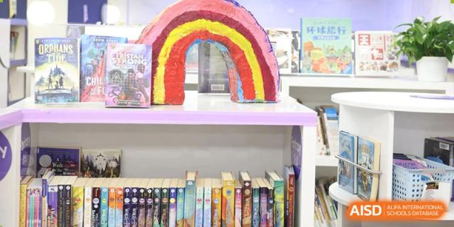 A bookshelf displaying books beneath a student-made rainbow craft at Yew Chung International School of Beijing.