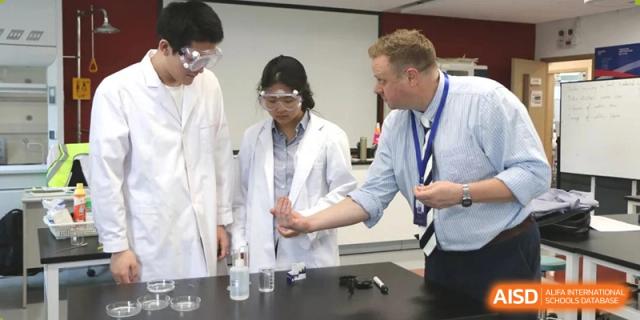 A science teacher assisting students in white lab coats with an experiment involving beakers at Yew Chung International School of Beijing.