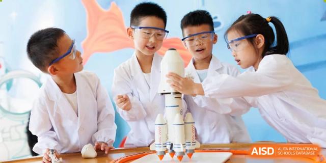Two students in lab coats and safety goggles proudly holding a model rocket in a science class at Yew Chung International School of Beijing.