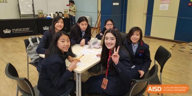 A group of happy students, one giving a peace sign, collaborating at a table in a classroom at Yew Chung International School of Beijing.