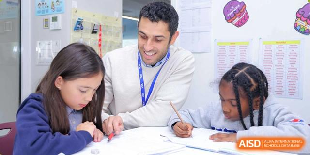 An adult teacher or mentor sitting at a table and working with students during a class at Yew Chung International School of Beijing.