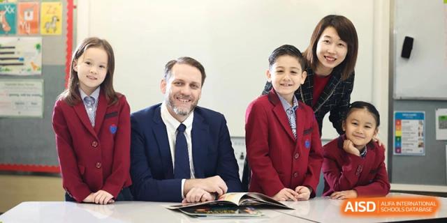 A teacher or administrator in a suit posing with a female student in school uniform at Yew Chung International School of Beijing.