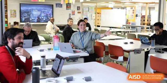 A teacher talking to students seated at a table, with a laptop and educational materials at Yew Chung International School of Beijing.