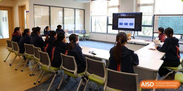 Students seated around tables in a large classroom or learning space during a lesson at Yew Chung International School of Beijing.