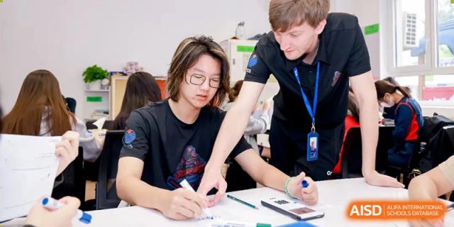 A male teacher assisting a student with a writing assignment or project at a table at Yew Chung International School of Beijing.