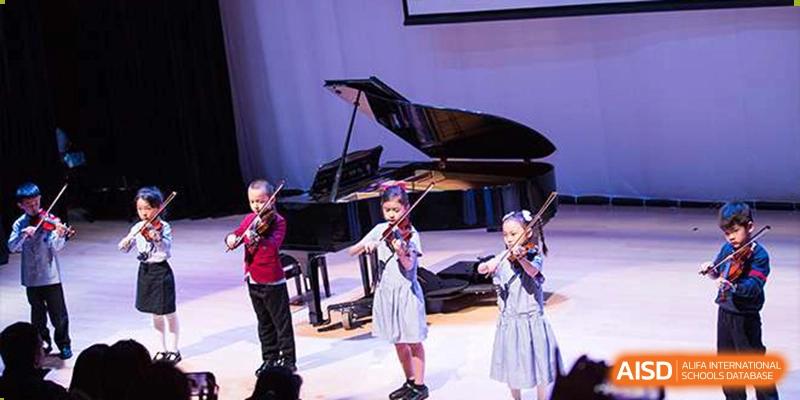 Students playing violins on stage next to a grand piano during a musical performance at Yew Chung International School of Beijing.