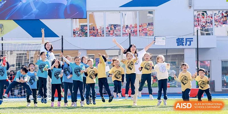 A group of happy students and a teacher running or cheering on a green field or playground at Yew Chung International School of Beijing.