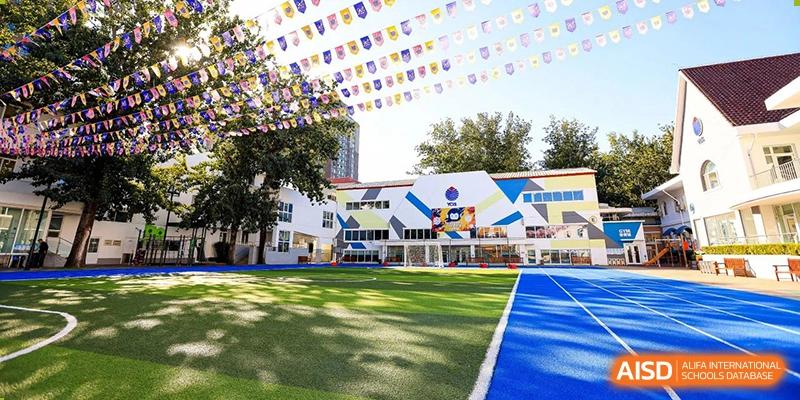 The colorful exterior of a school building with a well-maintained green lawn and playground at Yew Chung International School of Beijing.